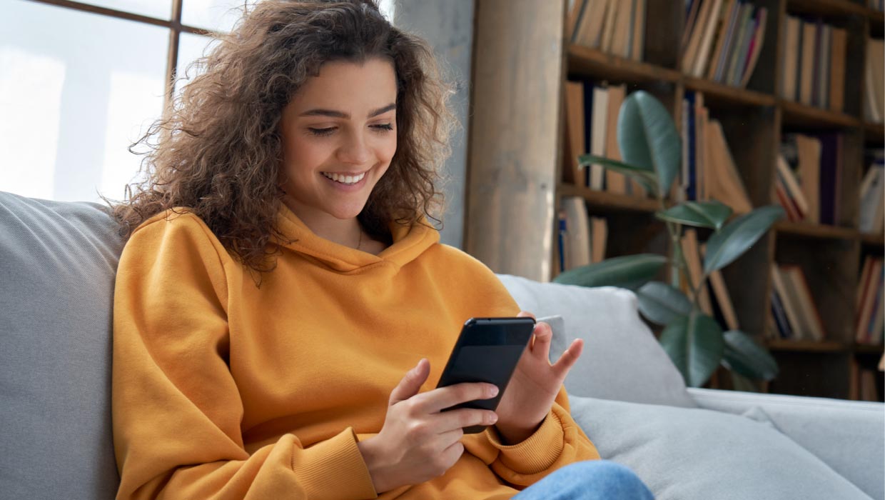 Junge Frau mit Handy und Pullover auf dem Sofa